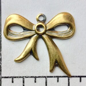Può includere: Ciondolo a forma di fiocco in metallo dorato con un anello in cima per attaccarlo a gioielli o artigianato.