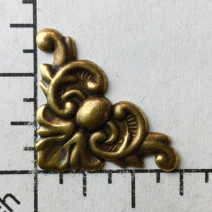 May include: A gold-toned metal corner accent with a floral design. The accent is about 1 inch in size.