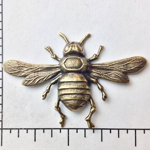 Pode incluir: Um amuleto de abelha de metal dourado com asas e pernas detalhadas. A abelha mede aproximadamente 2,5 cm de comprimento.