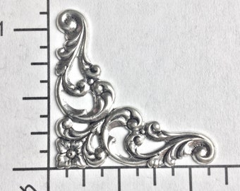 Può includere: Decorazione d'angolo in argento con un motivo floreale decorativo. La decorazione è di circa 2,5 cm.