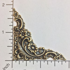 May include: A gold-toned metal corner accent with a floral design. The accent is approximately 1 inch in size.