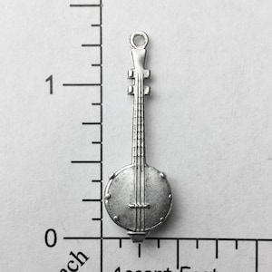 May include: Silver charm of a banjo, approximately 1 inch in length. The charm is detailed with a round body, a long neck, and strings.