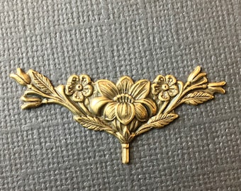 May include: A gold metal floral embellishment with a delicate design. The embellishment features three flowers and leaves.