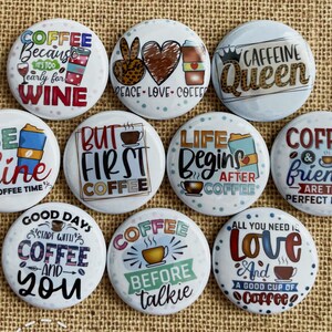 May include: A collection of white, round buttons with coffee-themed designs and text. The buttons feature phrases like "Coffee Because It's Too Early for Wine," "But First Coffee," and "Caffeine Queen." The buttons are on a burlap surface.