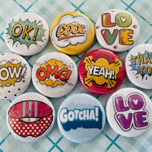 May include: Ten round, white, button pins with colorful comic book style designs. The pins feature phrases like "OK!" "Cool!" "Love" "Wow!" "OMG!" "Yeah!" "Thank You!" "Gotcha!" and "Love".