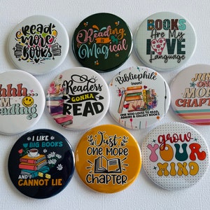 May include: A collection of ten round pinback buttons with various book-themed designs. The buttons feature phrases like "Read More Books," "Reading is Magical," and "Books Are My Love Language." Colors include white, black, green, yellow, and orange.