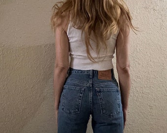 May include: A person wearing a white tank top and blue denim jeans. The jeans have a high waist and a straight leg.