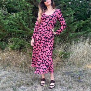 May include: A woman wearing a long-sleeved pink and black floral dress with a button-up front. She is wearing brown sandals and sunglasses.