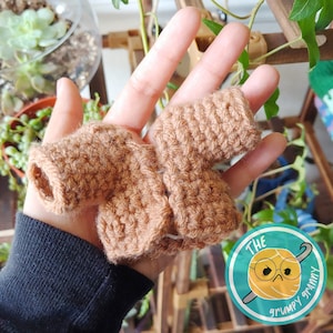 May include: A brown crocheted cardigan with a loose fit. The cardigan is held in a hand, with the fingers visible.