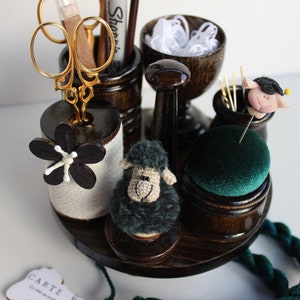 Könnte beinhalten: Ein Nähset aus Holz mit verschiedenen Fächern für Nadeln, Garn, Schere und andere Nähutensilien. Das Set enthält ein kleines schwarzes Schaf-Nähkissen, ein grünes Nähkissen und ein kleines Schweinchen-Nähkissen.
