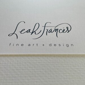Puede incluir: Primer plano de una superficie texturizada blanquecina con el nombre "Leah Frances" en elegante escritura negra. Debajo del nombre, el texto dice "fine art + design" en una fuente m&aacute;s peque&ntilde;a, sin serifa.