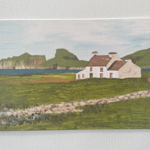 Puede incluir: Pintura de paisaje de una casa blanca con tejado marr&oacute;n, sobre un fondo de colinas verdes y un mar azul. Un muro de piedra recorre el primer plano, con un cielo azul claro. La obra est&aacute; enmarcada.