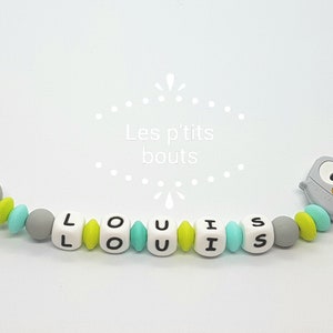 May include: A gray and green silicone baby teether with the name "LOUIS" spelled out in white beads. The teether has a gray owl charm and a clip for attaching to clothing.