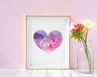 May include: A framed watercolor print of a pink and purple heart with the word "love" written in white cursive inside. The print is displayed on a white surface with a vase of pink and white flowers.