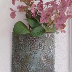 May include: A square, wall-mounted ceramic planter with a textured, mottled green and brown glaze. The planter holds a bouquet of pink hydrangea flowers with green leaves. The text FuzzyMudStudio.etsy.com is printed at the bottom.