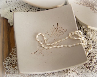 May include: A white ceramic dish with a floral design and a pearl necklace on top. The dish is on a white lace doily.