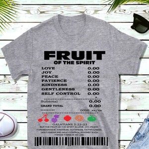May include: A gray t-shirt with black text that reads "FRUIT OF THE SPIRIT" and lists the fruits of the spirit with their corresponding values. The text "GALATIANS 5:22-23" is below the list, followed by a quote from the Bible verse.