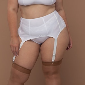 Op de afbeelding: Witte bh met kant en bijpassende jarretelgordel met bijpassende witte kousen. De jarretelgordel heeft aan elke kant drie banden en is gemaakt van een glad, satijnachtig materiaal.