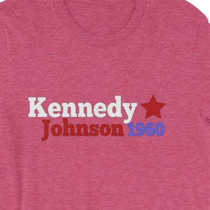 May include: A pink t-shirt with the text "Kennedy Johnson 1960" in white, blue, and red lettering with a red star.