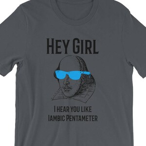 May include: A dark gray t-shirt with a black and white illustration of William Shakespeare wearing blue sunglasses. The text "HEY GIRL" is above the illustration and the text "I HEAR YOU LIKE IAMBIC PENTAMETER" is below the illustration.