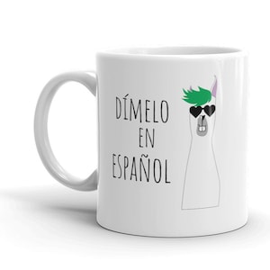 May include: White ceramic mug with a black and white illustration of a llama wearing sunglasses and a green mohawk. The text "DÍMELO EN ESPAÑOL" is printed on the mug.