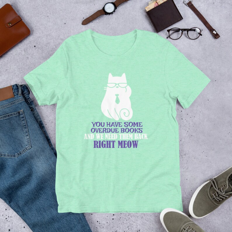 May include: A light green t-shirt with a white cat wearing glasses and a tie. The text on the shirt reads "You have some overdue books and we need them back right meow."