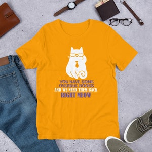 May include: A yellow t-shirt with a white cat wearing sunglasses and a tie. The text on the shirt reads "You have some overdue books and we need them back right meow."