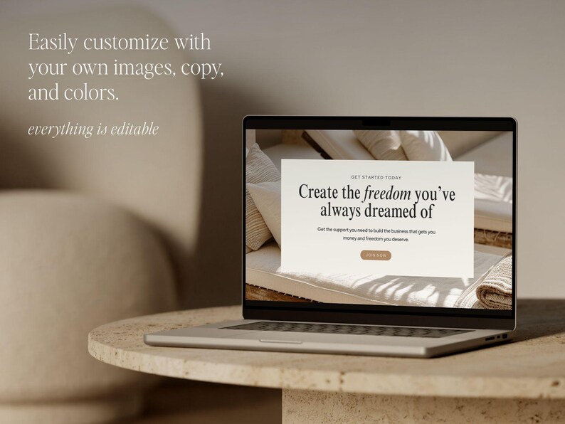 May include: A silver laptop shows a website mockup with the text "Create the freedom you've always dreamed of." The laptop is on a round, light-coloured stone table. The background is a neutral beige.