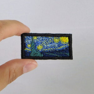 May include: A small embroidered patch featuring a recreation of Vincent van Gogh's "Starry Night" painting. The patch is framed with a black border and features a blue and yellow starry night sky with a green cypress tree in the foreground.