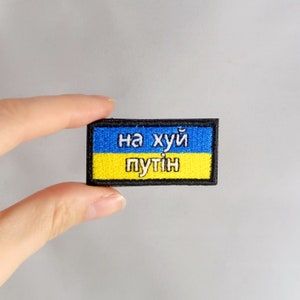 May include: A blue and yellow embroidered patch with the text "на хуй путин" in white.