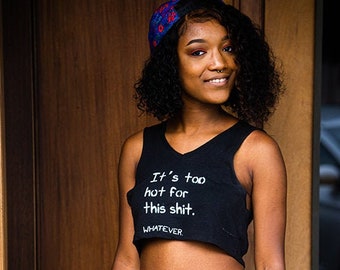 May include: Black crop top with the text "It's too hot for this shit. WHATEVER." The top is paired with black jeans. A patterned headband and a watch are also visible.