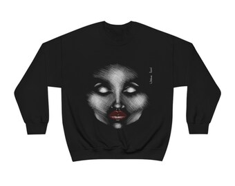 May include: Black sweatshirt featuring a detailed, grayscale sketch of a face with closed eyes and red lips. The artwork has a textured, cross-hatch style. The text "Welcome Angel" is printed vertically on the right side of the sweatshirt.