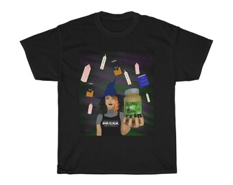 May include: Black t-shirt featuring a witch with a blue hat and orange hair holding a jar labeled "Witchy Not Bitcy". The shirt has a graphic of crystals and a book. The witch is wearing an apron that says "Whatever Apparel".