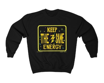 May include: Black sweatshirt with a yellow square design. The design features the text "KEEP THE SAME ENERGY" in yellow, with a lightning bolt and various small doodles. The sweatshirt is a crew neck style.