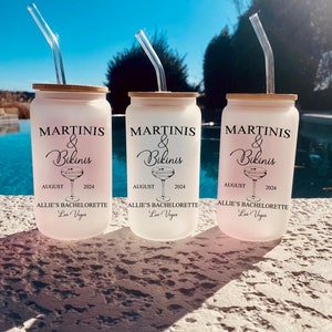 May include: Three white frosted tumblers with black text and a martini glass graphic. The text reads "Martini's & Bikinis" with the date "August 2024" and "Allie's Bachelorette Las Vegas". Each tumbler has a clear plastic straw.