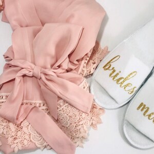 Könnte beinhalten: Eine rosa Satin-Morgenmantel mit Spitzenbesatz und ein passender weißer Morgenmantel mit goldenen Buchstaben, auf dem "bridesmaid" steht.