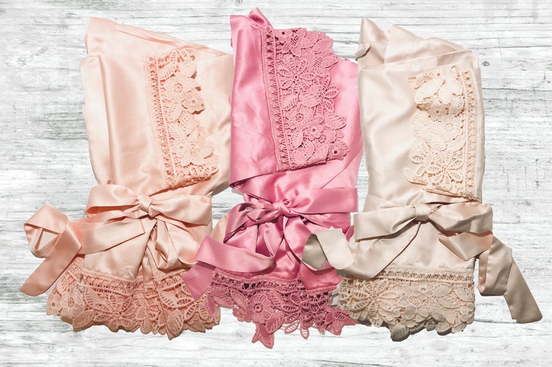 May include: Three satin robes with lace trim in pink, blush, and ivory colours. The robes are tied at the waist with matching satin sashes.