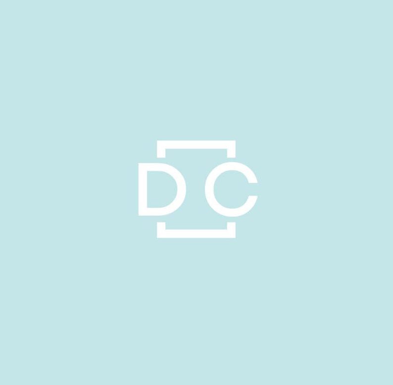 May include: A white logo on a pale blue backdrop. The logo comprises the letters "D" and "C" in a sans-serif typeface, contained within a rectangular frame. The design is minimalist and contemporary.