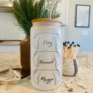 May include: A frosted glass water bottle with a bamboo lid and a clear reusable straw. The bottle has three dog silhouettes with the names "Troy", "Hannah", and "Maggie" printed on them.