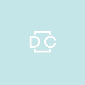 May include: White logo on a light blue background. The logo features the letters "D" and "C" in a sans-serif font, enclosed within a rectangular frame. The design is simple and modern, with a minimalist aesthetic.