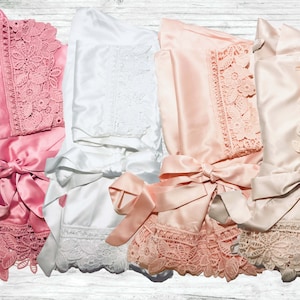 May include: Four satin robes with lace trim in pink, white, and peach colours. The robes have a sash tie and are folded in a pile.
