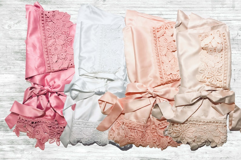 May include: Four satin robes with lace trim in pink, white, and peach colours. The robes have a sash tie and are folded in a pile.