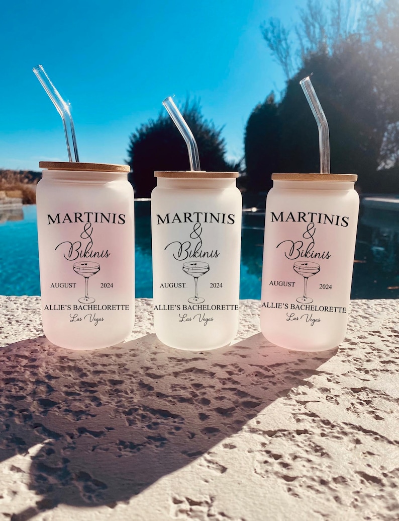 May include: Three white frosted tumblers with black lids and clear straws. Each tumbler has a black graphic of a martini glass and the text "Martinis & Bikinis" with the dates "August 2024". The text "Allie's Bachelorette Las Vegas" is printed on the bottom of each tumbler.