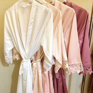 May include: Three satin robes with lace trim in white, blush pink, and dusty rose.