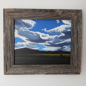 Puede incluir: Una pintura enmarcada de un paisaje con un cielo azul y nubes blancas. La pintura est&aacute; en un marco de madera r&uacute;stico.