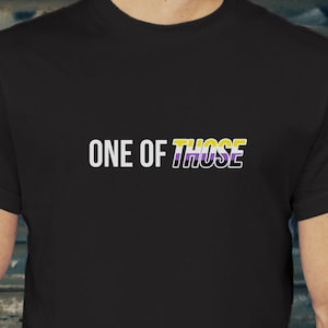Op de afbeelding: Zwart T-shirt met de tekst "ONE OF THOSE" in wit met een geel, paars en zwart streepontwerp.
