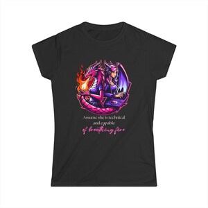 May include: Black t-shirt with a graphic of a woman with a dragon. The woman is sitting at a computer and the dragon is breathing fire. The text "Assume she is technical and capable of breathing fire" is printed below the graphic.