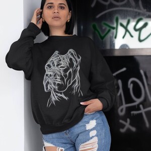 Op de afbeelding: Een zwart sweatshirt met een wit lijnkunstontwerp van een Cane Corso hondenkop. Het model draagt ​​het sweatshirt met een blauwe jeans.