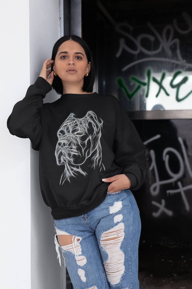 Op de afbeelding: Een zwart sweatshirt met een wit lijnkunstontwerp van een Cane Corso hondenkop. Het model draagt ​​het sweatshirt met een blauwe jeans.