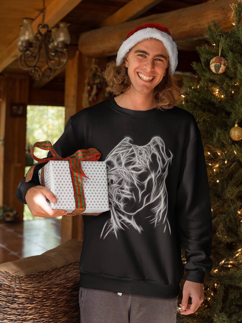 Op de afbeelding: Een zwart sweatshirt met een witte afbeelding van een gestileerd hondenhoofd. De persoon die het sweatshirt draagt, glimlacht en houdt een ingepakt cadeau vast.